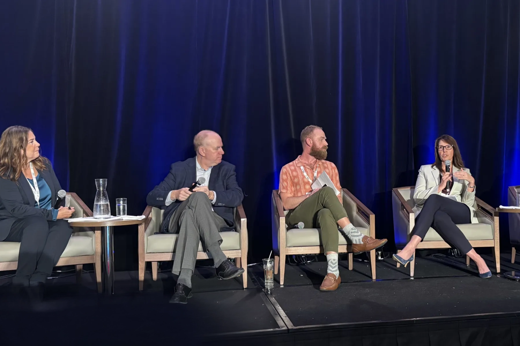 Panel of people sitting on stage having a discussion with a blue backdrop.